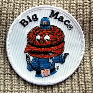 May include: White circular embroidered patch with the words "Big Mac" and a cartoon character wearing a blue uniform and a hat with the letter "M" on it.