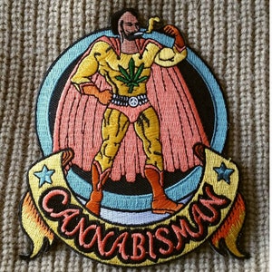May include: Embroidered patch featuring a superhero figure in a yellow and orange costume with a cannabis leaf emblem. The patch includes the text "CANNABISMAN" on a banner, with a blue, black, and pink background. The figure is smoking a pipe.