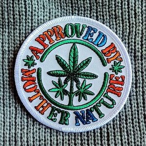 May include: White embroidered patch with a green marijuana leaf design and the text "APPROVED BY MOTHER NATURE" in a rainbow color scheme.