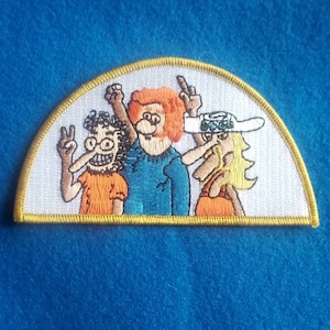 May include: A white embroidered patch with a yellow border in the shape of a half-circle. The patch features three cartoon characters with peace signs, one with a blue shirt, one with an orange shirt, and one with a white hat and orange shirt.