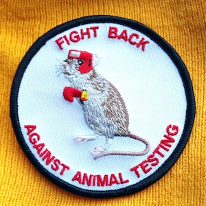May include: White embroidered patch with a red boxing mouse wearing a red headband and red boxing gloves. The text "FIGHT BACK AGAINST ANIMAL TESTING" is in red around the mouse.