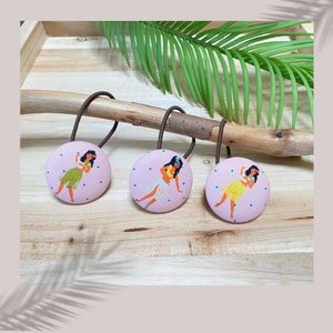 Könnte beinhalten: Drei rosafarbene Haargummis mit weißem Tupfenmuster und einem Hula-Mädchen-Design. Jedes Haargummi zeigt ein anderes Hula-Mädchen mit einer Blumenkette und einer Blume im Haar.
