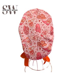 May include: Pink surgical scrub hat with a pattern of pink and orange cowboy boots and hats. The hat has a tie on the back.