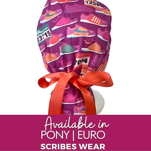 May include: A purple scrub cap featuring a repeating pattern of colorful running shoes and race bibs with visible numbers like 23715 and 12586. The cap is secured at the back with a bright orange satin ribbon tied into a bow, creating a gathered fit.