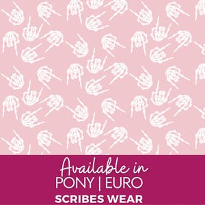 May include: Pink background with a repeating pattern of white skeleton hands making the rock and roll hand gesture. The bottom of the image has text that reads "Available in PONY | EURO SCRIBES WEAR."