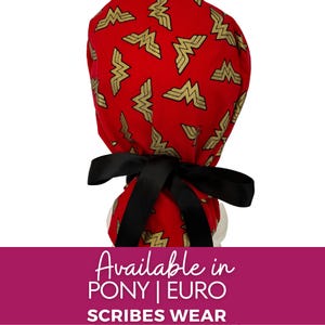 May include: A red scrub cap featuring a repeating gold Wonder Woman logo pattern. The cap includes a black ribbon tie at the back for adjustment. The text at the bottom reads: Available in PONY | EURO SCRIBES WEAR. The design is consistent and vibrant.