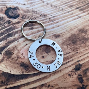 May include: Silver keyring with a round tag engraved with the coordinates "24.30. N 84.79. W".