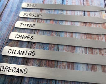 Könnte beinhalten: Sechs silberne Pflanzenmarkierer aus Metall mit den eingravierten Namen "Salbei", "Petersilie", "Thymian", "Schnittlauch", "Koriander" und "Oregano".