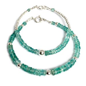 May include: Two silver bracelets with green gemstone beads. The larger bracelet has a silver bead at the clasp. The smaller bracelet has a silver bead at the clasp and a silver bead in the center.