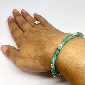 May include: A green gemstone bracelet with silver beads. The bracelet is on a person's wrist.