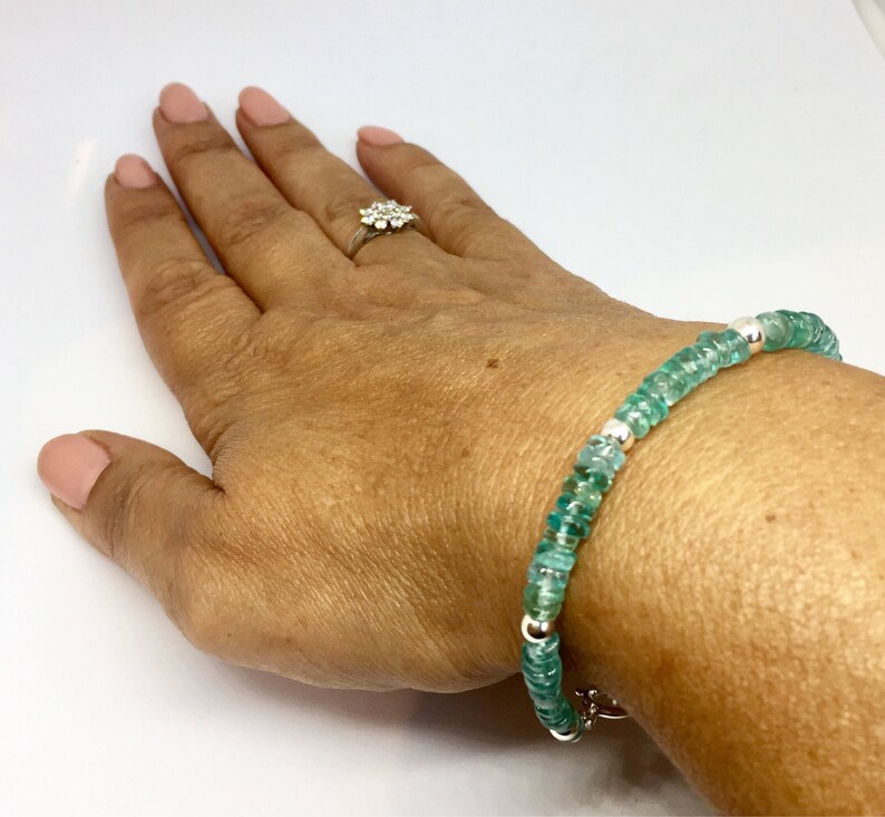 May include: A green gemstone bracelet with silver beads. The bracelet is on a person's wrist.