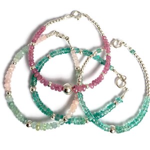 May include: Three silver beaded bracelets with pink, green, and light blue gemstones. The bracelets are layered on top of each other.