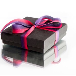 May include: A black gift box with a purple and pink ribbon tied in a bow.