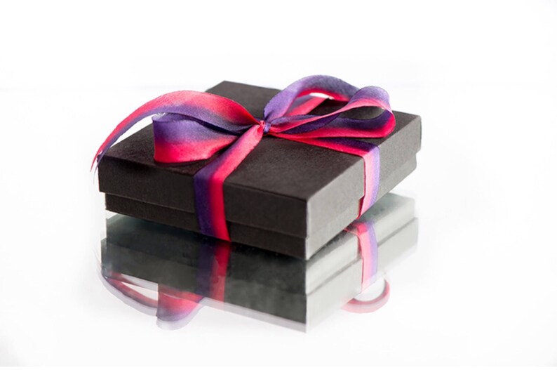 May include: A black gift box with a purple and pink ribbon tied in a bow.