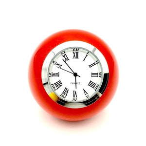 May include: A red round clock with Roman numeral markings on a white face. The clock says "QUARTZ" below the face.