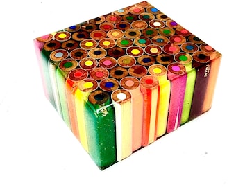 May include: A cube-shaped art piece made from numerous colored pencils. The pencils are arranged vertically, showcasing their colorful tips on top and sides. The piece is set against a white background.