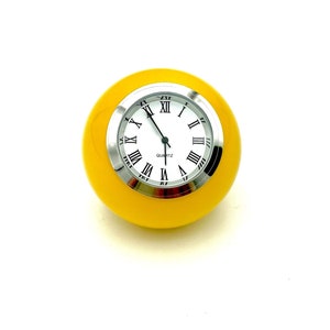 May include: A yellow round clock with Roman numeral markings and a silver face. The clock says "QUARTZ" on the face.