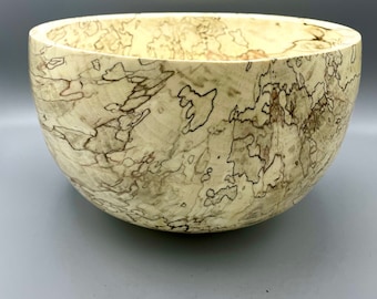 May include: A large, round wooden bowl with a natural wood finish. The bowl has a unique, swirling grain pattern in shades of brown and beige.