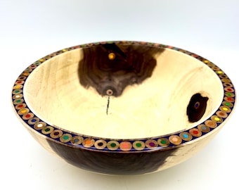 May include: A wooden bowl with a light-colored interior and a dark brown exterior. The rim is decorated with a colorful mosaic of pencil tips. The bowl has a natural wood grain pattern and a smooth finish.