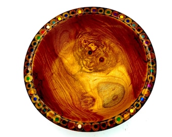 May include: A handcrafted wooden bowl with a rich, warm brown and golden interior. The rim is adorned with a decorative border of colorful, inlaid circles. The bowl's interior features unique wood grain patterns, making it a distinctive decorative piece.