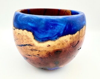 May include: A handcrafted wooden bowl with a striking design. The top section is a vibrant blue, transitioning to a natural wood grain with brown and tan hues. The bowl's interior is a deep, rich brown.
