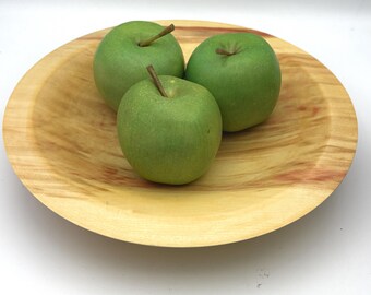 May include: Three green apples in a wooden bowl. The bowl is light brown with reddish brown streaks. The apples are arranged in a triangular shape.