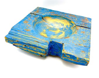 May include: A square, rustic wooden bowl with a shallow, circular indentation. The bowl is painted in a distressed blue with gold accents, showcasing the natural wood grain. The bowl has a unique, weathered appearance.