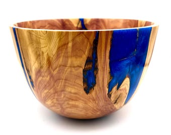 May include: A wooden bowl with a natural wood grain exterior and a vibrant blue resin interior. The bowl's design features a smooth, rounded shape, showcasing the contrast between the light wood and the deep blue resin.