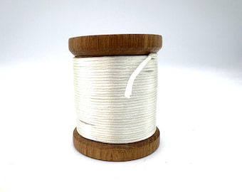 May include: A wooden spool with white thread. The spool has a dark brown, circular base and top, with the thread wound tightly around the center. A white thread end is visible.