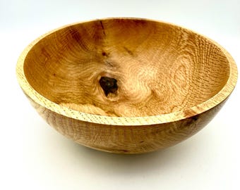 May include: A large, wooden bowl with a natural, light brown finish. The bowl has a smooth, rounded interior and a slightly flared rim.
