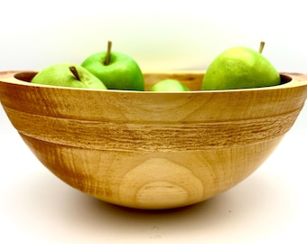 May include: A wooden bowl with a natural finish, filled with green apples. The bowl has a wide rim and a rounded bottom.