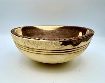 May include: A handcrafted wooden bowl with a light-colored exterior and a dark, swirling interior. The rim is inlaid with colorful pencil tips. The bowl has a smooth, rounded shape with carved horizontal lines around the exterior.