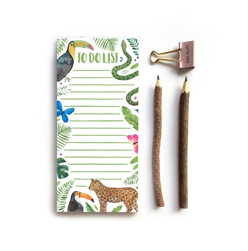 Op de afbeelding: Een notitieblok met een tropisch thema met een illustratie van een toekan, luipaard en slang, met de woorden "TO DO LIST" bovenaan. Twee potloden met een takachtig uiterlijk en een roze paperclip met de woorden "LOVE THIS" zijn ook inbegrepen.