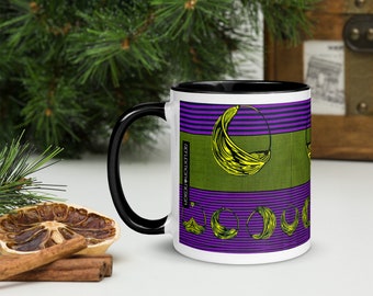 May include: White ceramic mug with a black rim and handle. The mug features a purple and green geometric pattern with yellow crescent shapes. The text "REFLEXION BY DESIGN" is printed on the side of the mug.