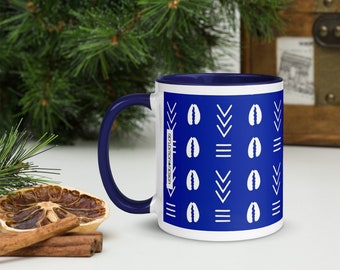 May include: White coffee mug with a blue rim and a blue and white geometric pattern. The pattern features white cowrie shells and white chevron shapes on a blue background. The text "RELEVENTHA DESIGN" is printed on the side of the mug.