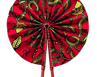 May include: A circular folding hand fan featuring a vibrant red fabric base with a repeating pattern of yellow and black floral and leaf motifs. The fan is constructed with pleated fabric and includes two brown handles that fold together at the base.