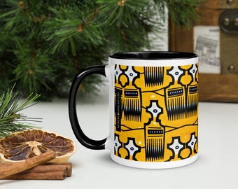 May include: A white ceramic mug with a black rim and handle. The mug features a yellow and black pattern of combs and geometric shapes. The text "REFLEXION DESIGN" is printed on the side of the mug.