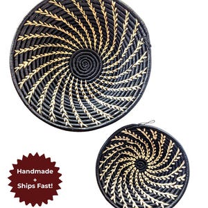 Könnte beinhalten: Zwei schwarz-beige gewebte Körbe mit einem Spiralmuster. Der größere Korb ist rund, und der kleinere hat eine Schlaufe zum Aufhängen. Die Körbe sind handgefertigt.