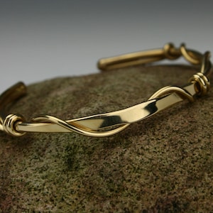 May include: A gold bangle bracelet with a twisted design. The bracelet is made of a single piece of metal that is twisted and then formed into a circle.