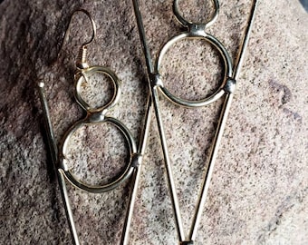 May include: A pair of gold-toned earrings with a geometric design. Each earring features two circles and a triangle shape.