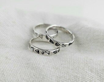 May include: Three silver rings with a geometric pattern of triangles. The rings are stacked on top of each other.