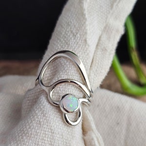 May include: A silver ring with an abstract design featuring a white opal gemstone.