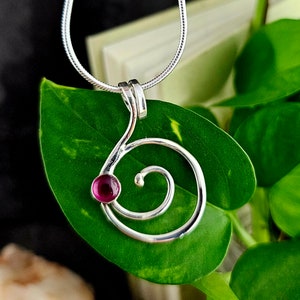May include: A silver necklace with a spiral pendant featuring a small, round, pink gemstone.