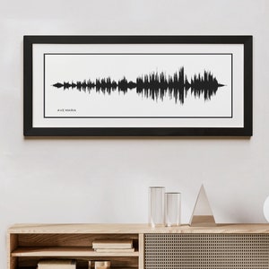 May include: A black framed print of a sound wave with the text "AVE MARIA" underneath. The print is hanging on a white wall above a wooden shelf with a vase of dried flowers and two clear glass cylinders.