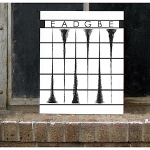 May include: A white rectangular print featuring five black abstract shapes, each resembling a tornado, with the letters E, A, D, G, and B above them. The print is set against a window and brick wall.