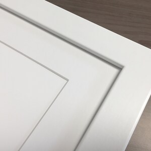 Puede incluir: Primer plano de una puerta de armario blanca con un dise&ntilde;o de panel elevado. La puerta tiene un aspecto simple y limpio y est&aacute; hecha de un material liso y plano.