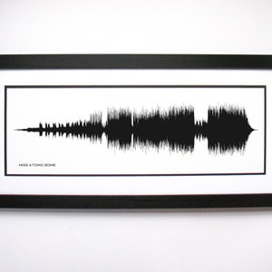 May include: Black framed print featuring a black and white sound wave design. The sound wave is displayed on a white background, with the text "MISS ATOMIC BOMB" at the bottom. The frame is rectangular.