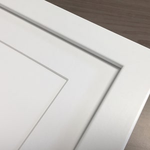 May include: Close-up of a white painted cabinet door with a raised panel design. The door has a simple, clean look.