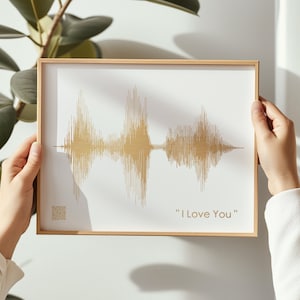 以下が含まれることがあります： 「I Love You」という文字の下に、金色の音波が描かれた額装されたプリント。プリントは人の手で持たれている。