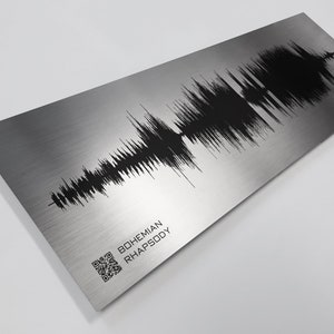 May include: A silver metal print with a black sound wave graphic and the text "BOHEMIAN RHAPSODY". A QR code is in the lower left corner.